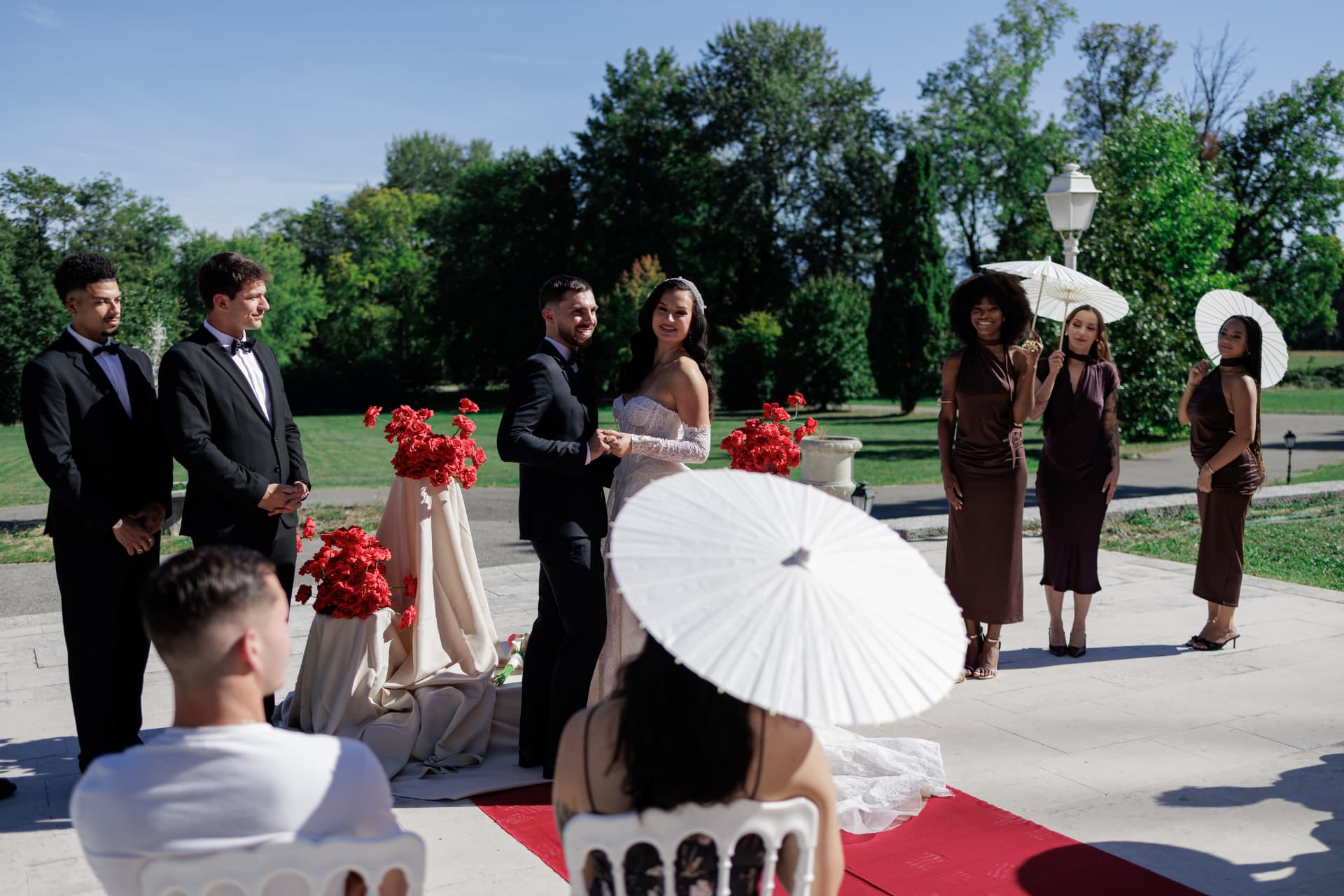 Cérémonie dans le parc du Château de Crassy : les mariés face à leurs témoins, ombrelles blanches et bouquets de roses rouges